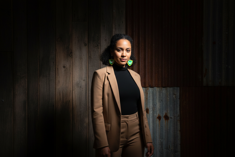 Woman in a brown coat standing against a dark, textured wall.