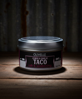 Jar of Olivelle Taco on a wooden surface with a dark background