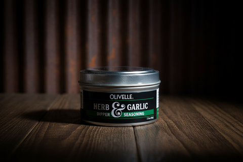 Olivelle Herb & Garlic seasoning container on a wooden surface with a dark background