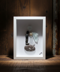 Framed artwork with stones and a piece of glass on a wooden shelf