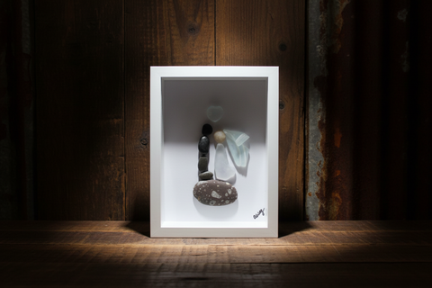 Framed artwork with stones and a piece of glass on a wooden shelf