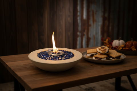 Fire pit bowl with flames on a wooden table, surrounded by pumpkins and gourds.