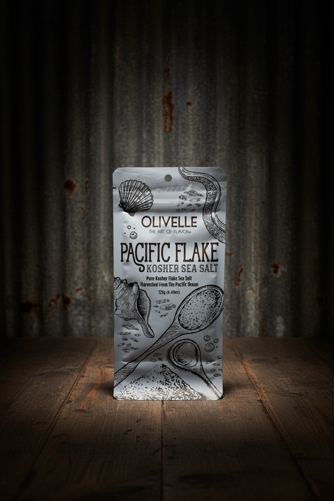 Olivelle Pacific Flake Kosher Sea Salt packaging on a rustic wooden surface with corrugated metal background