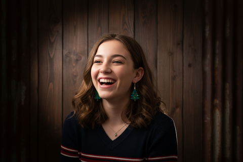 Woman, wearing Christmas tree earrings, laughing with a wooden panel background