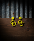 Yellow earrings with 'OU' design on a wooden surface and corrugated metal background