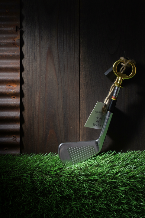 Golf club with a key and dollar bill on grass next to a wooden surface
