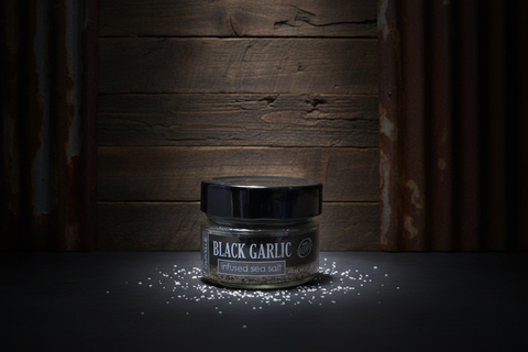 Jar of black garlic on a dark surface with wooden background