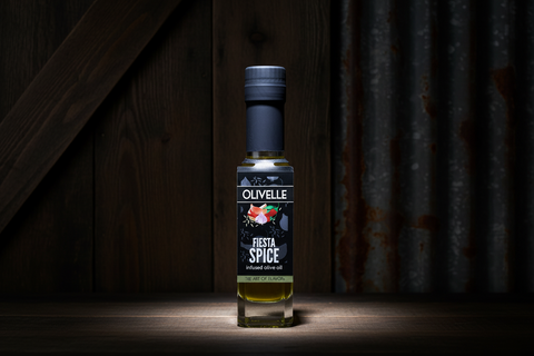 Bottle of Olavelle Fiesta Spice oil on a wooden surface with a dark background