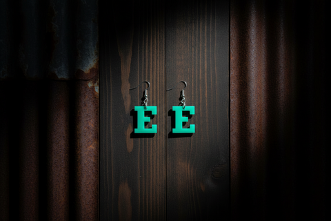 Green letter 'E' earrings on a dark wooden background