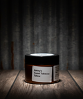 Jar of 'Kenny's Sweet Tobacco Tallow' on a wooden surface with a dark background